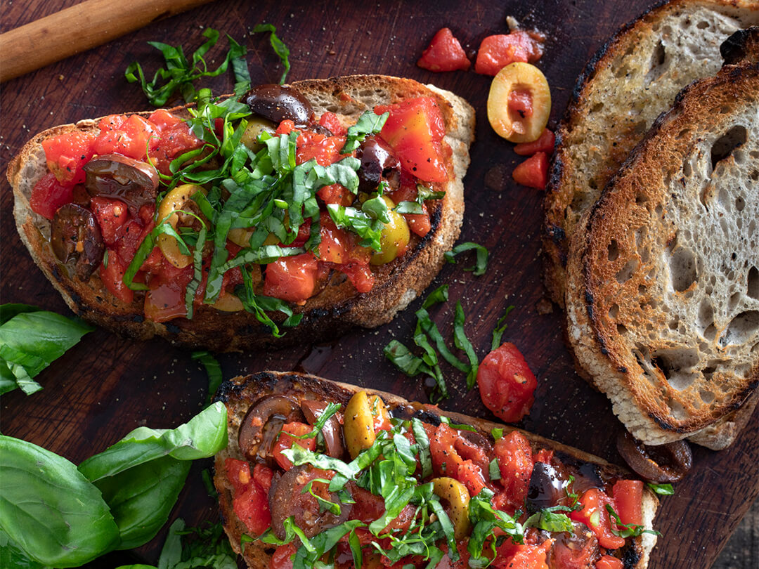 Bruschetta de tomate cubeteado con cubierta de aceitunas, hojas de albahaca y aceite de oliva